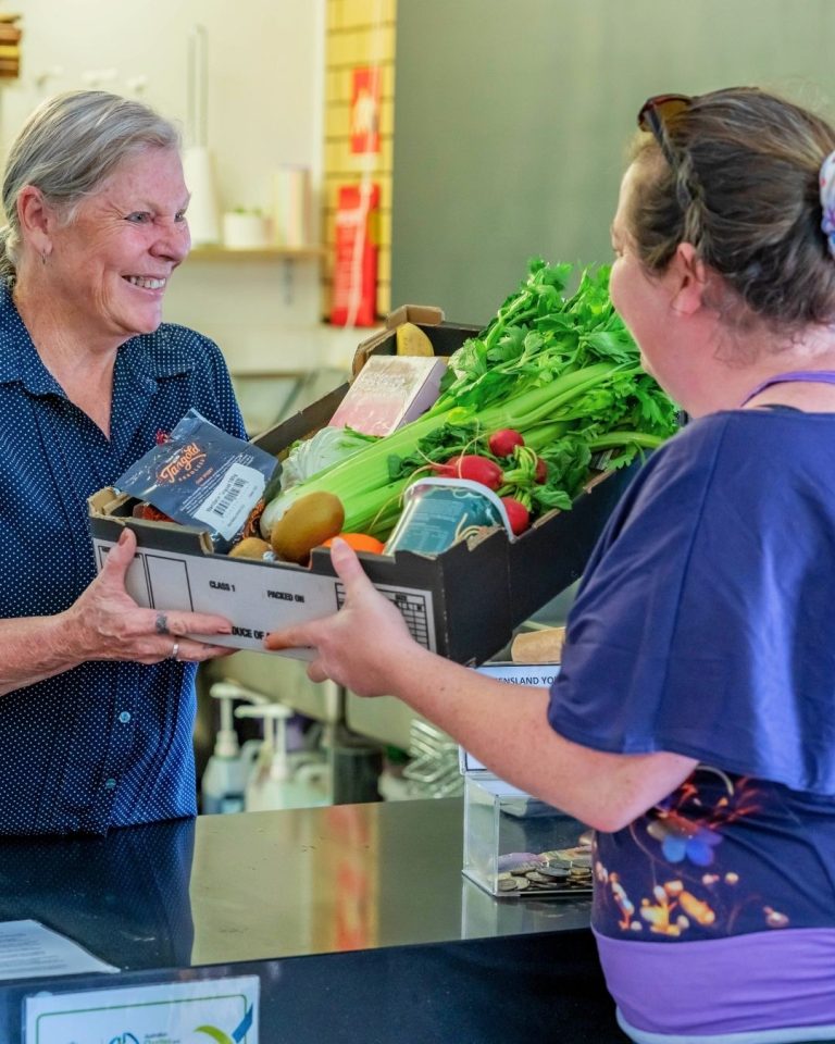 Smiling woman passes a box of rescued vegetables across a counter to a customer at a community pantry