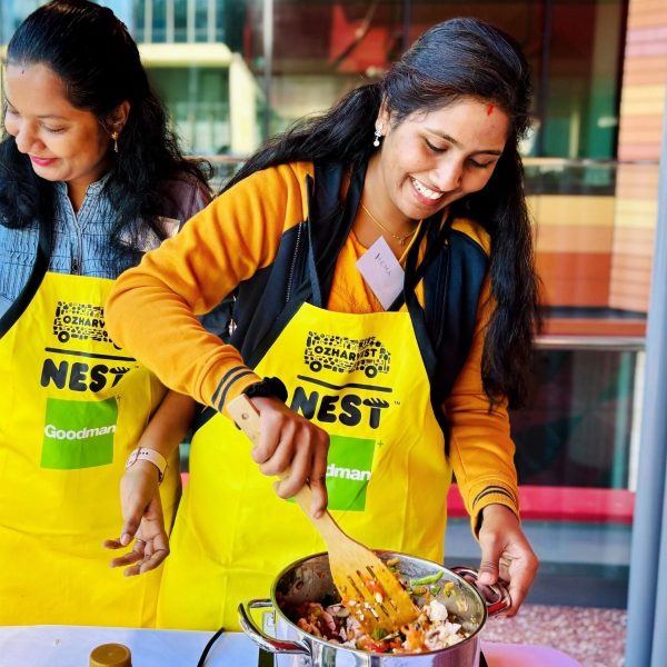 Two women in yellow OzHarvest NEST aprons stirring a pot of vegetables at an outdoor cooking session