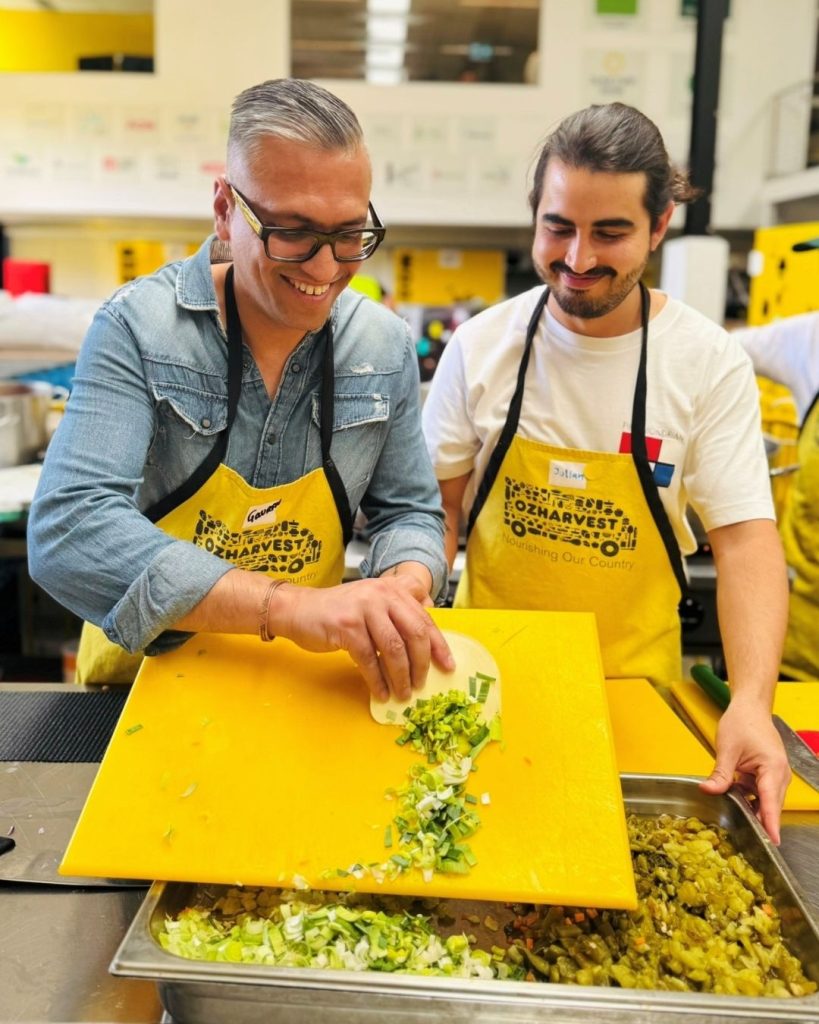 Two volunteers in OzHarvest aprons chopping greens together at a Cooking for a Cause session