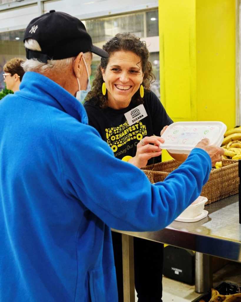 OzHarvest Market volunteer handing a meal to an older shopper at a free community market
