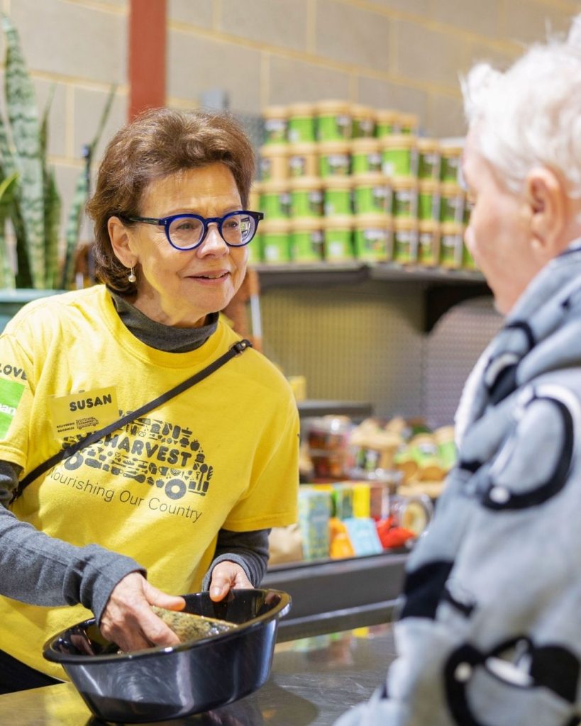 OzHarvest volunteer Susan in yellow tee serving a customer at a community food market