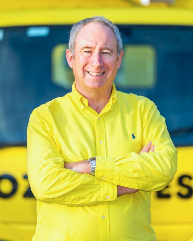 OzHarvest CEO in a bright yellow shirt smiles with arms crossed in front of a yellow OzHarvest van