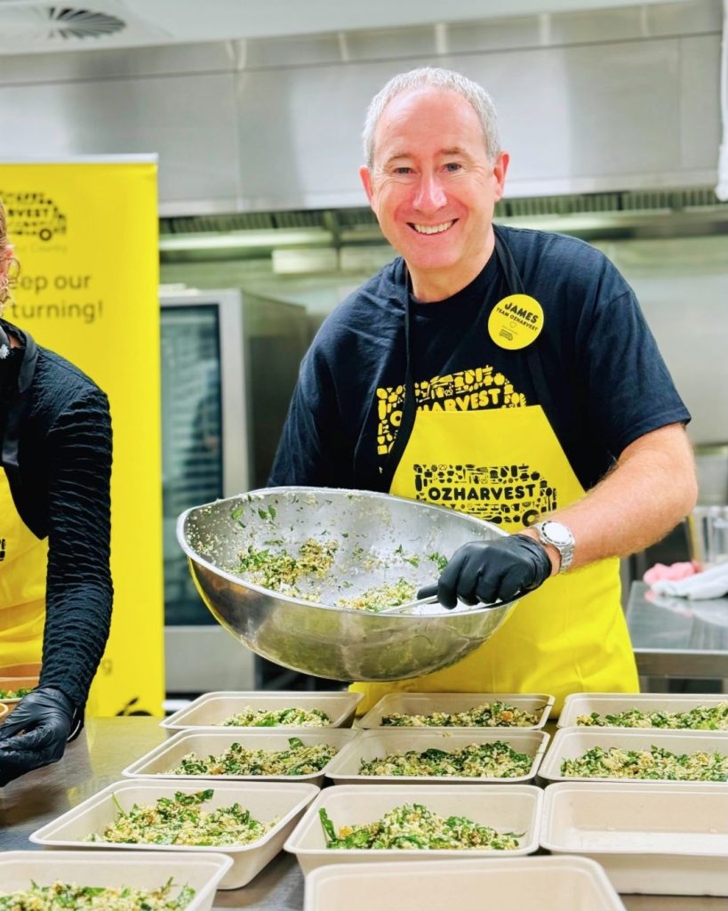 OzHarvest CEO James Goth tosses a large bowl of salad while packing meal trays in a kitchen