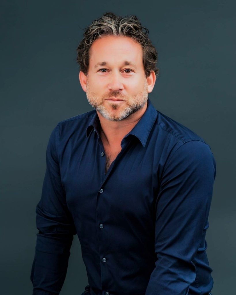Studio portrait of OzHarvest Chair in a navy shirt against a dark teal background