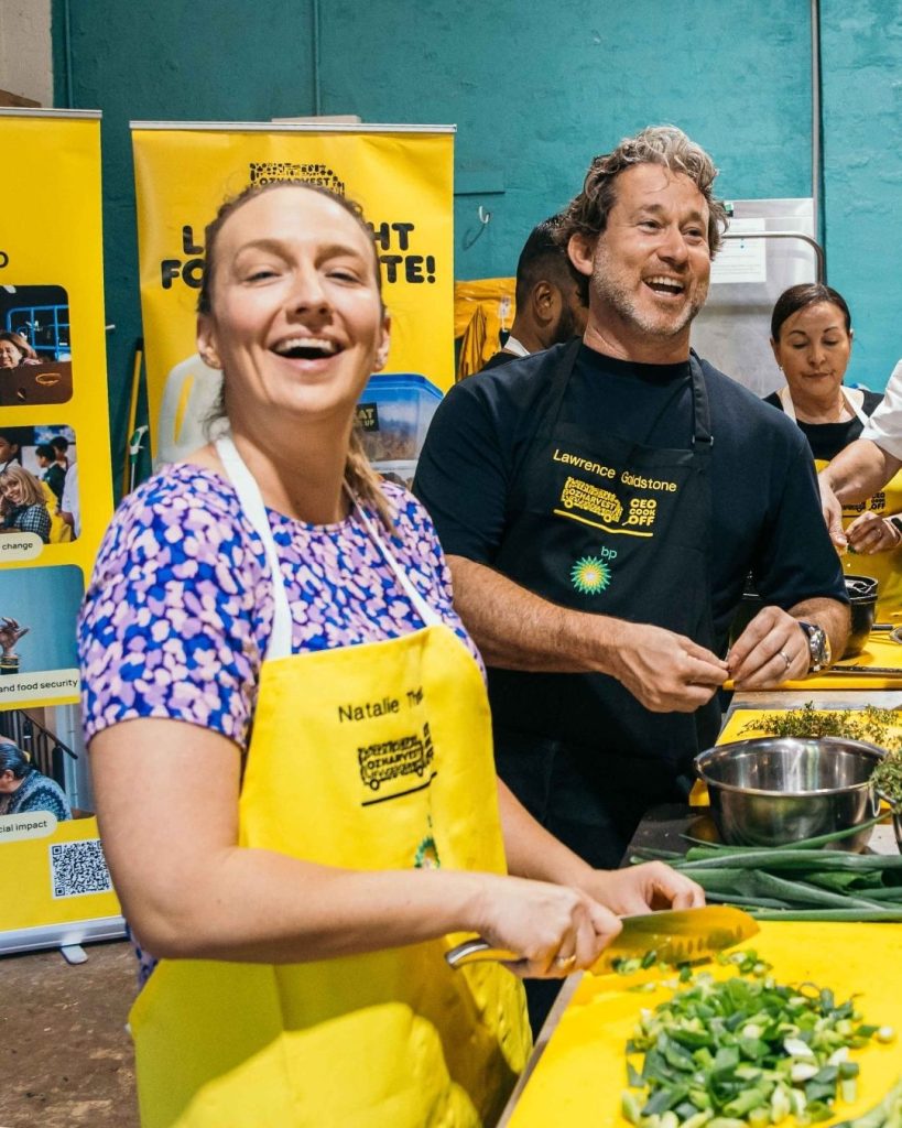 OzHarvest Chair Lawrence Goldstone laughs beside a volunteer chopping spring onions at the CEO Cook Off