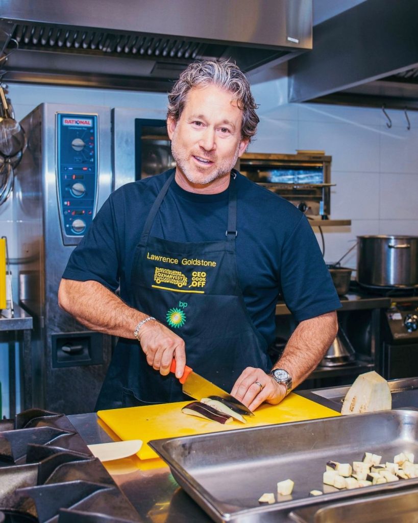 OzHarvest Chair Lawrence Goldstone slices eggplant on a yellow board in a commercial kitchen