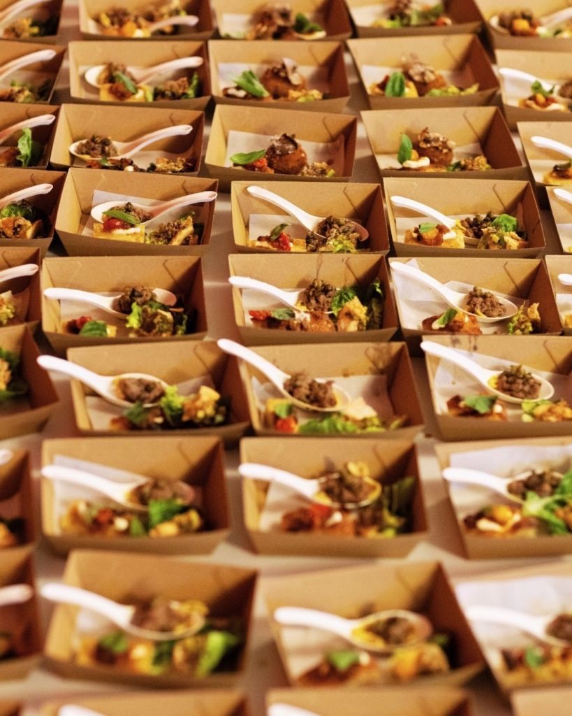Rows of catering canapes in kraft paper boxes with white tasting spoons at an OzHarvest event