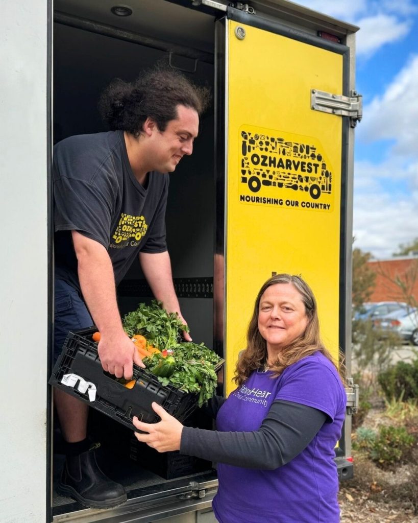 OzHarvest volunteers loading a crate of rescued vegetables from a yellow refrigerated truck