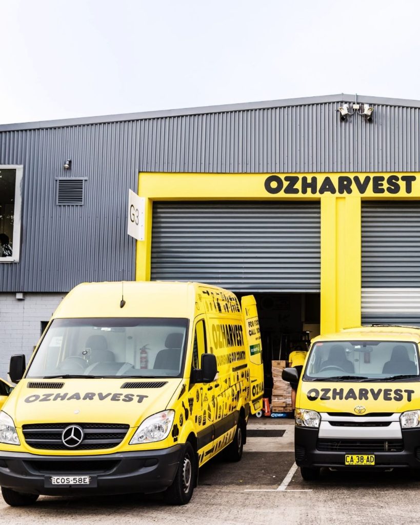 Yellow OzHarvest delivery van and Toyota van parked outside the branded OzHarvest depot building