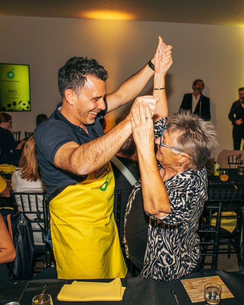 Man in a yellow OzHarvest apron high-fiving an older woman at a celebratory event
