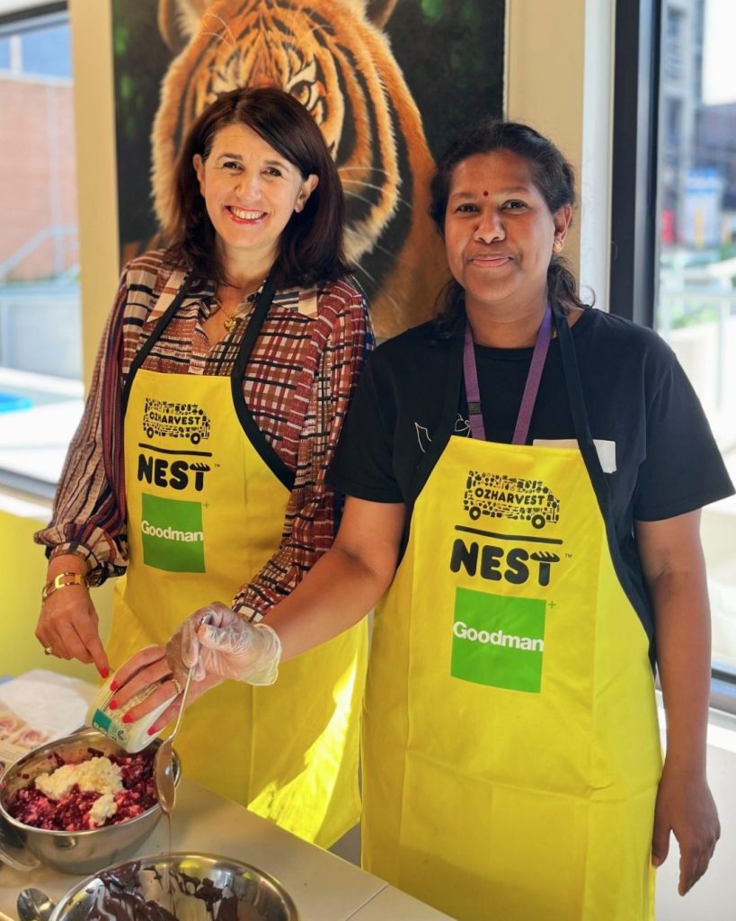 Two women in OzHarvest NEST aprons preparing food together in front of a tiger mural