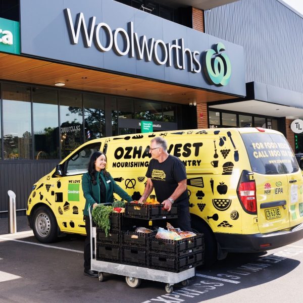 OzHarvest staff load crates of produce from a trolley into a yellow van outside a Woolworths store