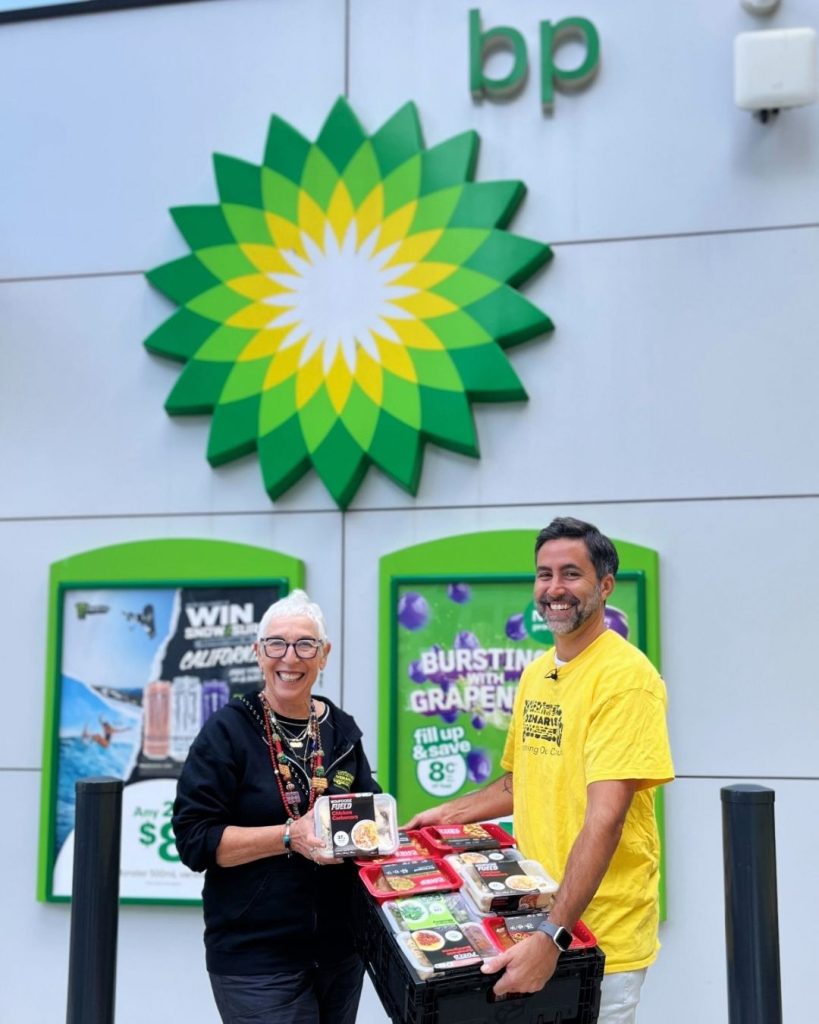 Two OzHarvest volunteers carrying rescued ready meals outside a BP service station