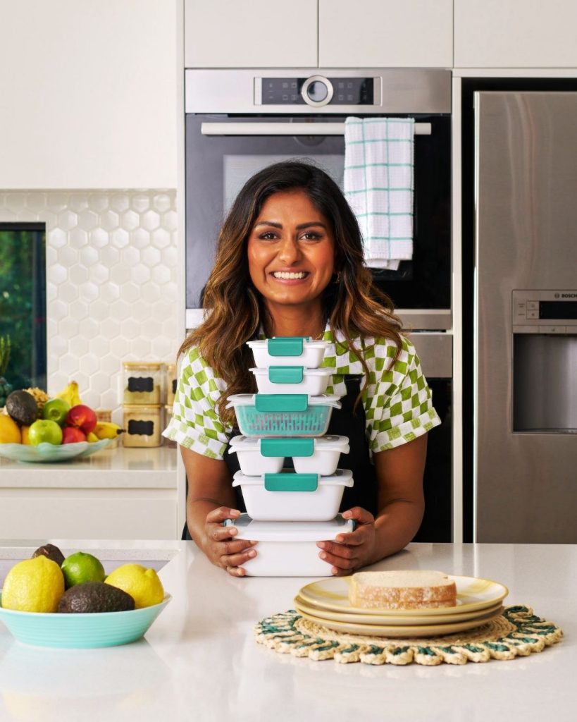 Smiling woman in a modern kitchen holding a stack of teal and white food storage containers