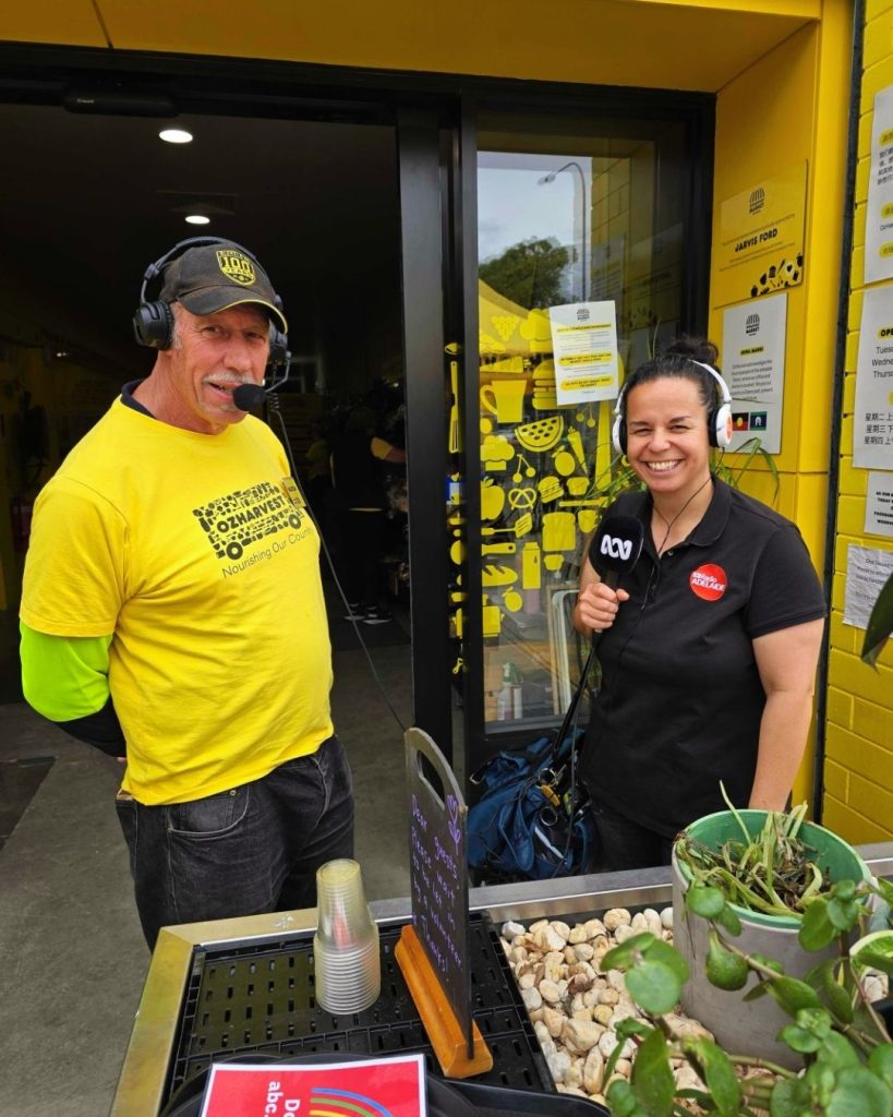 OzHarvest volunteer in a yellow shirt being interviewed by an ABC radio reporter at an event