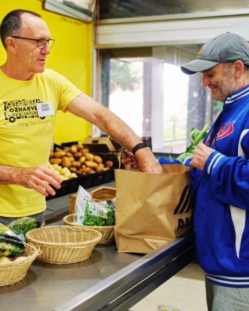 OzHarvest volunteer handing a bag of rescued vegetables to a man at a community food market