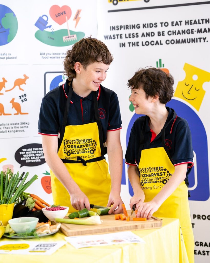 Two students in OzHarvest FEAST aprons chopping vegetables together at a healthy cooking workshop