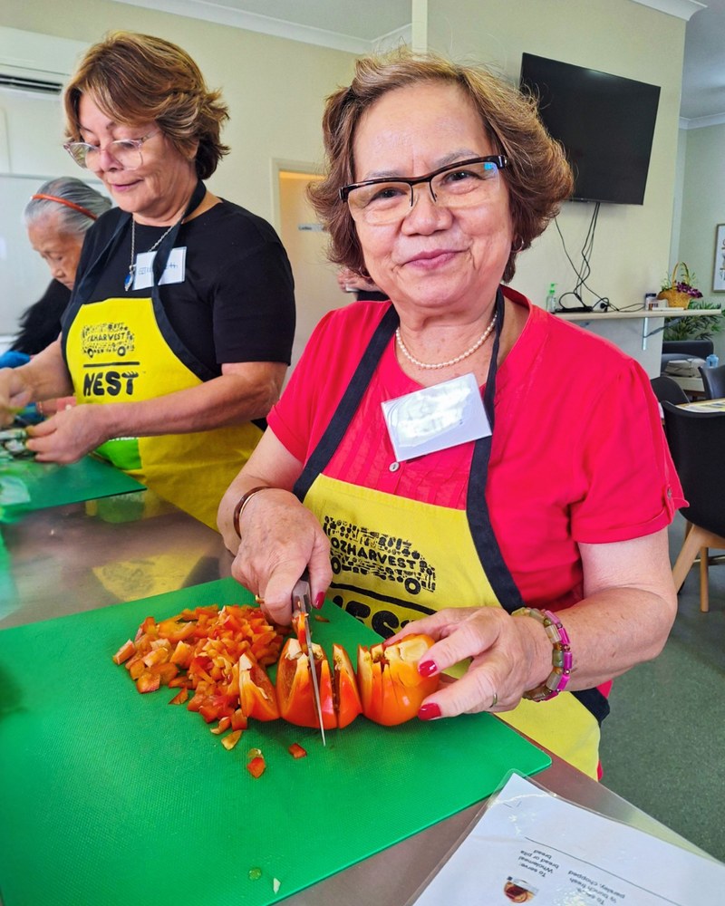 Woman in OzHarvest NEST apron chopping tomatoes on a green board in a community cooking class